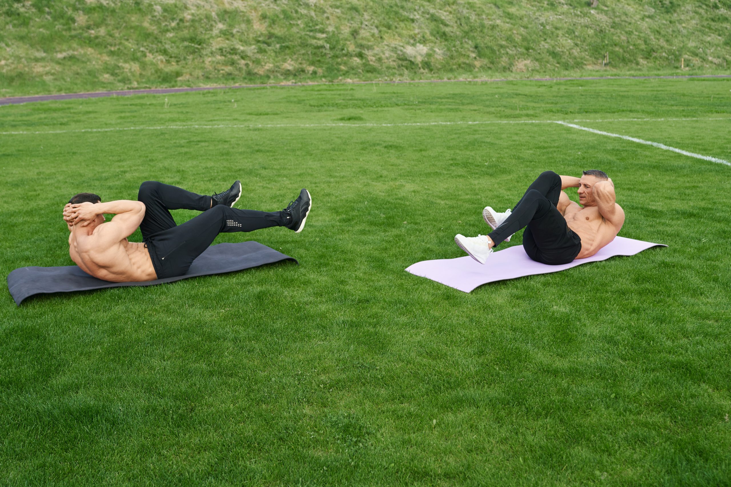 Athletes performing bicycle crunch ab workout outdoors on a sports field